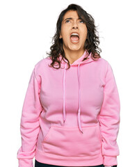 Young hispanic woman wearing casual sweatshirt angry and mad screaming frustrated and furious, shouting with anger. rage and aggressive concept.