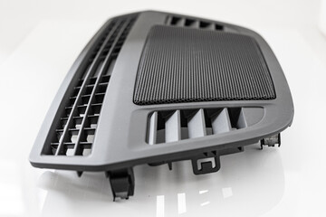 Part of car dashboard for directing airflow of the HVAC system with grill for hifi loudspeakers between the openings placed on white reflective background.