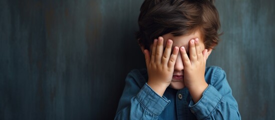 A Caucasian child, looking sad and fearful, is covering their face with their hands while making a stop gesture, conveying embarrassment and negativity. - obrazy, fototapety, plakaty