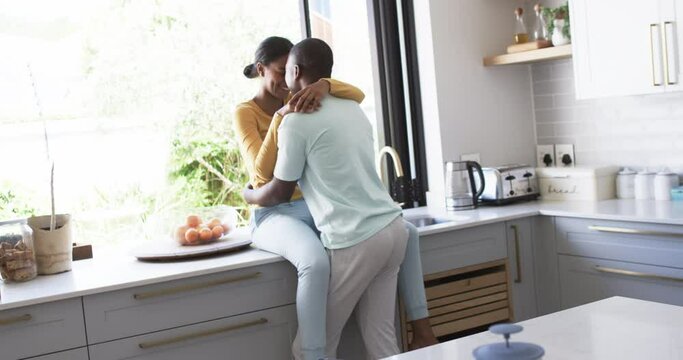 A diverse couple shares an affectionate moment in a modern kitchen, hugging