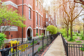 Moderrn brick row houses with bay windows along a fenced paved path running along the side of a public park. A high rise block of flats is in background.