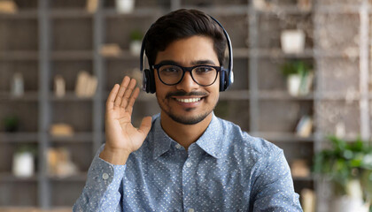  Friendly and helpful man wearing headset device and smart casual shirt looks at the camera and greeting interlocutor, support representative in touch, hindu guy in headphones involved meeting
