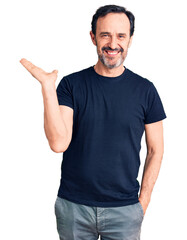 Middle age handsome man wearing casual t-shirt smiling cheerful presenting and pointing with palm of hand looking at the camera.