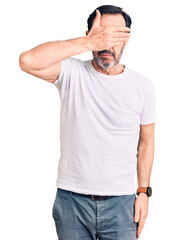 Middle age handsome man wearing casual t-shirt covering eyes with hand, looking serious and sad. sightless, hiding and rejection concept