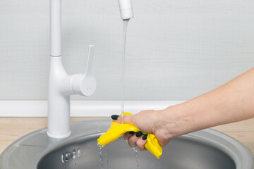 female hand wets a rag under running water in the kitchen