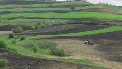 Obraz premium Tractor plowing the field on green hills, beautiful panorama landscape in countryside