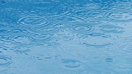 Rain drops falling making circle ripples at the surface of blue water