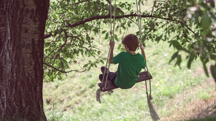 Naklejka na ściany i meble Silhouette of kid in wooden swing with ropes hanging from old big tree branch