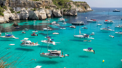 Picturesque panorama of Cala Macarella in Menorca Spain, with yachts floating on turquoise sea - obrazy, fototapety, plakaty