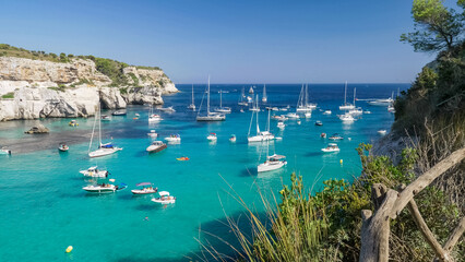 Many white yachts float on turquoise waters of Cala Macarella in Menorca Island Spain