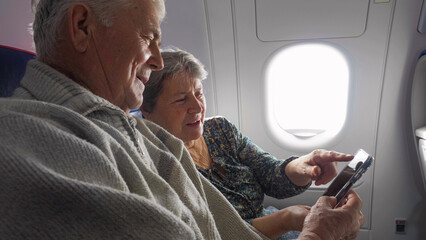 Elderly man and woman couple watching the mobile phone in airplane