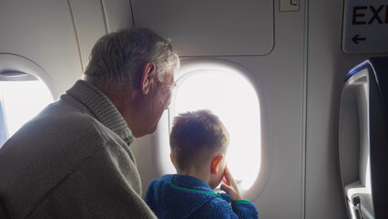 Little kid and grandfather looking on window in airplane