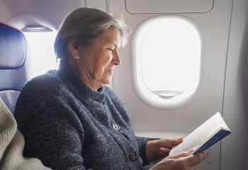 Elderly woman enjoys reading a book in the airplane during the flight