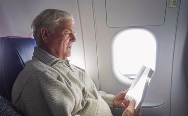 Elderly man reading a book in the airplane during the flight