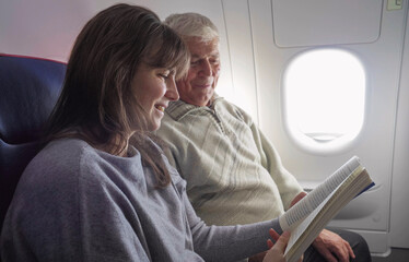 Young woman and her elderly father read a book in the airplane during the flight
