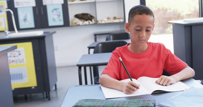 In a school classroom, a young African American student is focused on writing, with copy space