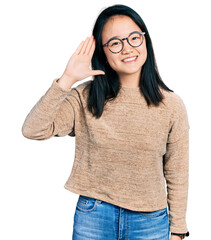 Fototapeta premium Young chinese woman wearing casual sweater and glasses waiving saying hello happy and smiling, friendly welcome gesture