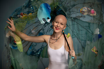 A joyful bald woman is surrounded by a variety of colorful fish props and netting, creating a playful undersea atmosphere