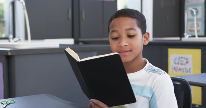 In school, in the classroom, a young African American student reads a book