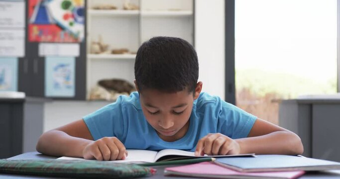 In school, in a classroom, a young biracial student concentrates on reading