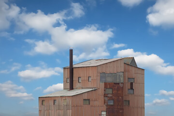tall building of an old factory with a chimney against a background of blue sky with clouds