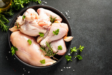 Chicken wings, drumsticks and breast with herbs and spices on black background. Top view with copy space.