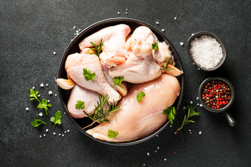 Chicken wings, drumsticks and breast with herbs and spices on black background. Top view with copy space.