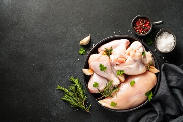Raw Chicken with herbs and spices. Different part of chicken - fillet, wings, drumsticks. Flat lay on black background.
