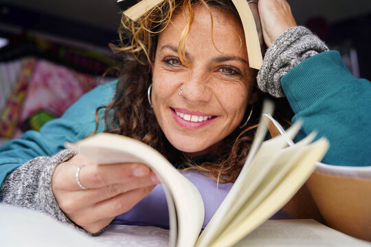 A funny woman reading a book laying on the bed. World book day - Powered by Adobe