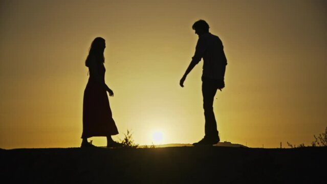 A captivating silhouette of a couple walking from the frame's edge to meet and embrace at the center against a sunset backdrop