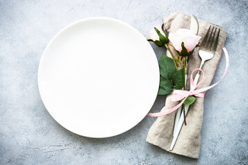 White plate, cutlery and wine glass with pink flowers. Spring table settong. Flat lay with copy space.
