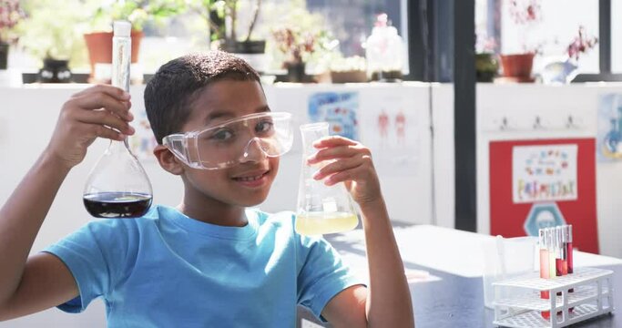 In school, in the classroom, a young African American student examines chemical flasks