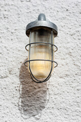 Lit lamp/lantern on exterior of building against a white textured wall in the day light 