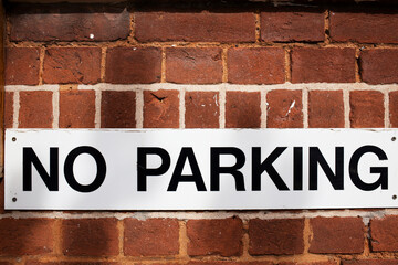 No Parking sign against red brick wall under subtle dappled light 