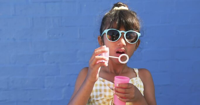 In school, a young biracial student blows bubbles against a blue background