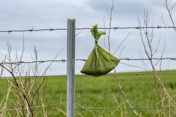 A bag of dog poop abandoned on a barbed wire fence