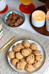 Cup of tea or coffee, stack of books, e-reader, glasses, various cookies, almonds, orange juice and lit candles on the table. Hygge at home. Selective focus.