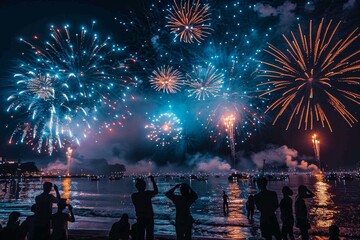 A multitude of sparklers light up the night as a crowd watches from a beach, creating a mesmerizing scene
