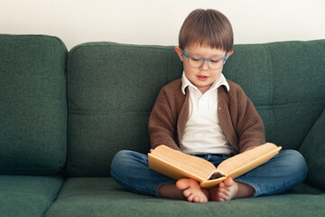 a child with a book on the couch, a boy wearing glasses reading a book
