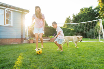 Young mother and son plays soccer with dog and have fun together. Happy family playing football...