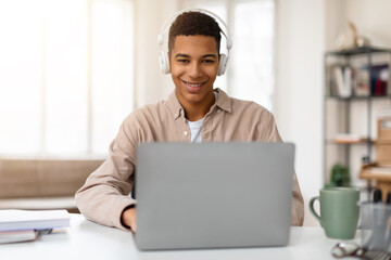 Smiling african american teen guy with headphones using laptop