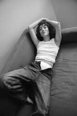sexy fashionable young curly-haired woman in jeans and white T-shirt lies on the blue sofa against the white wall of the house. showing white pants.
