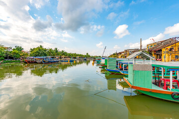 Wooden boats on the Thu Bon River in Hoi An Ancient Town (Hoian), Vietnam. Yellow old houses on...