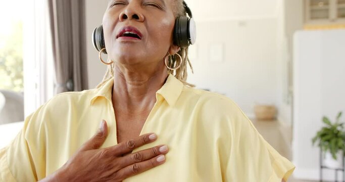 An African American senior woman mediating and wearing headphones with closed eyes at home