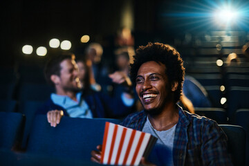 Smiling young man watching a movie in theater with popcorn