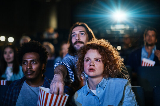 Group of diverse young people watching a movie in cinema with popcorn