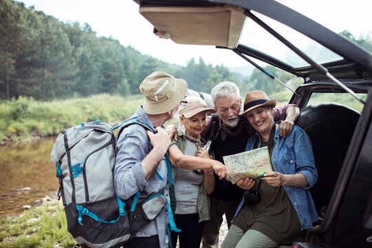 Elderly friends planning a hike with a map by the car