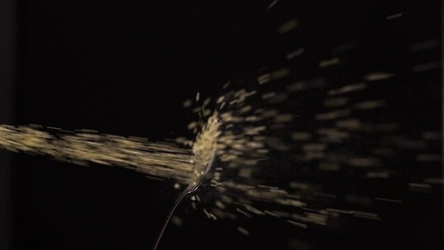 Slow motion of sprinkling sugar from spoon in dark studio