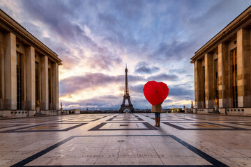 Concept of Paris travel concept with a woman holding a heart shaped umbrella in front of the Eiffel Tower during sunrise