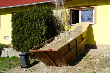 A large metal container full of construction debris near the window of a house under repair